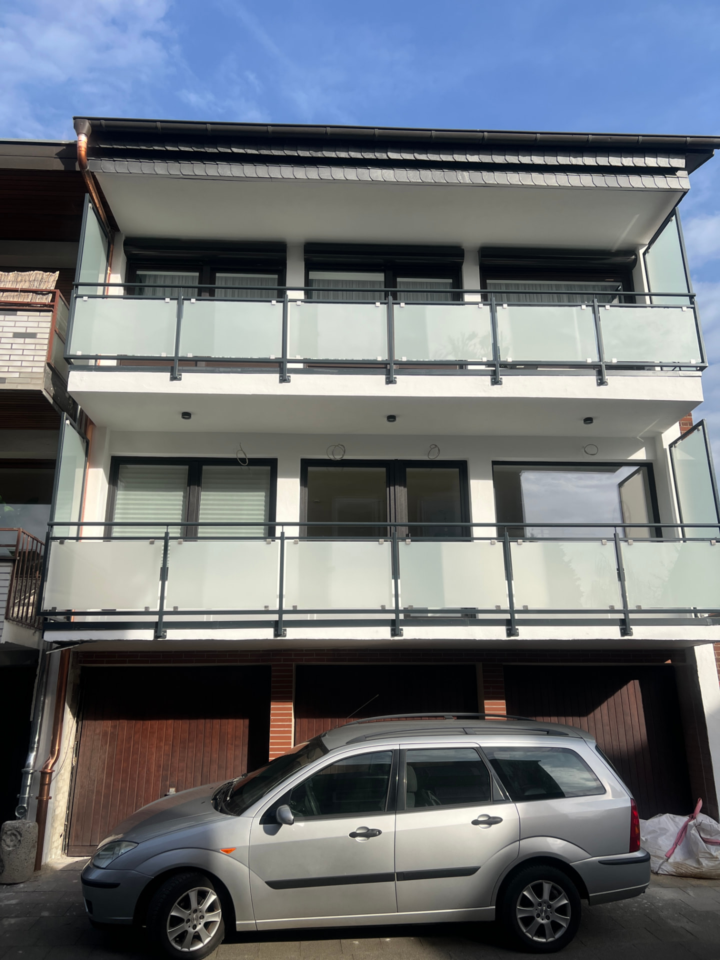 Fertiggestellte helle Wohnhausfassade mit dunklen Fenstern und Glasbalkonen