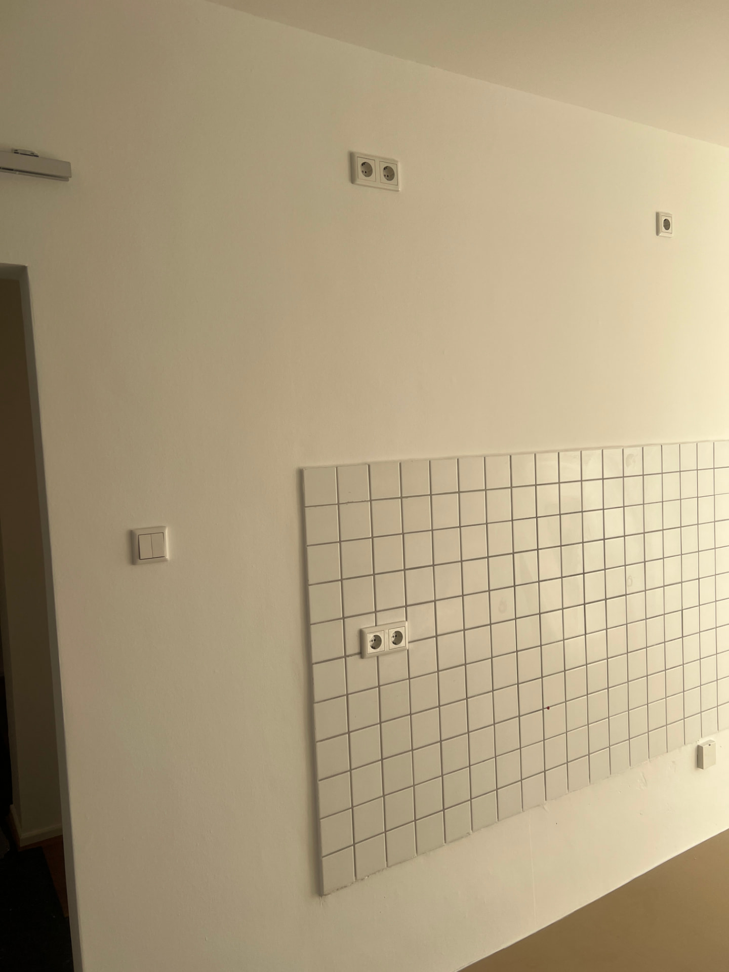 Frisch gestrichene helle Wand mit Fliesenspiegel und Steckdosen